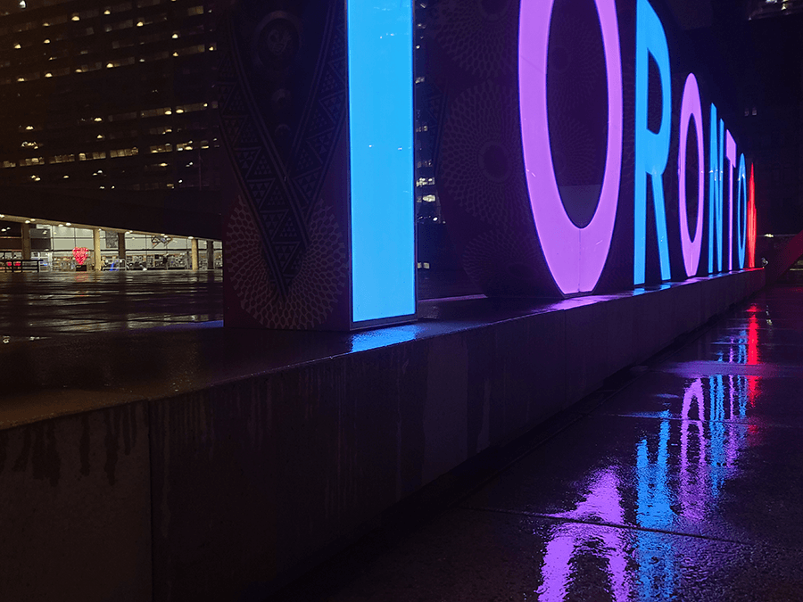 Low angle shot of 3D Toronto sign and reflection of it, lit purple and blue.