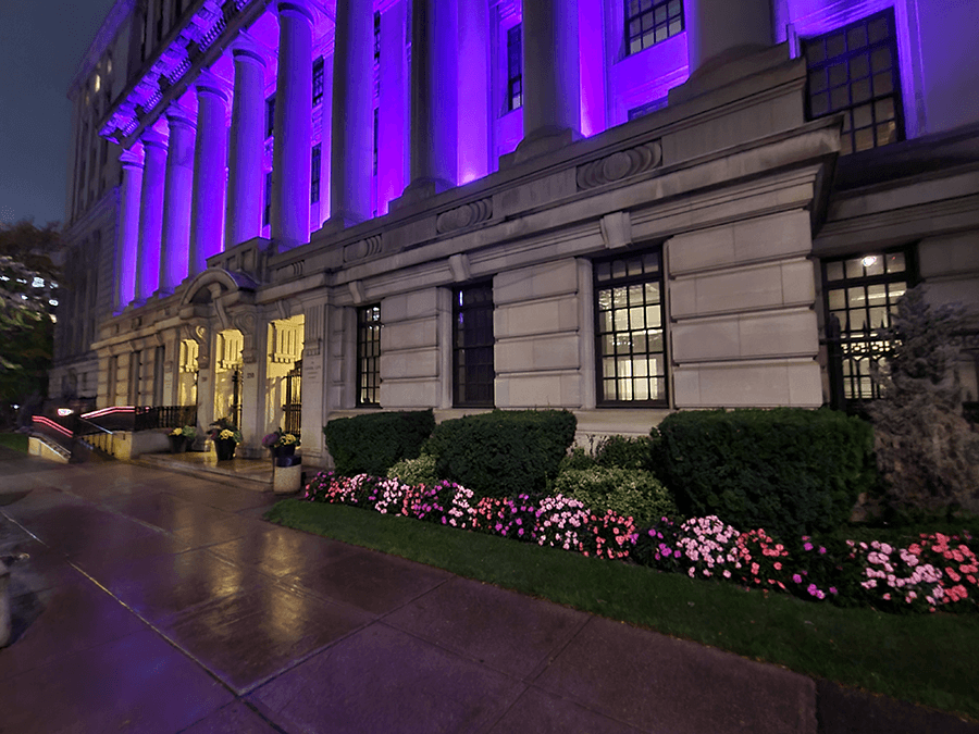 Street-level close angle view of the Canada Life Building illuminated purple for Light It Up! For NDEAM